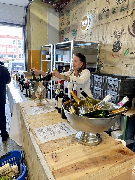 Eine Frau steht hinter einer langen Tafel und verkauft Wein